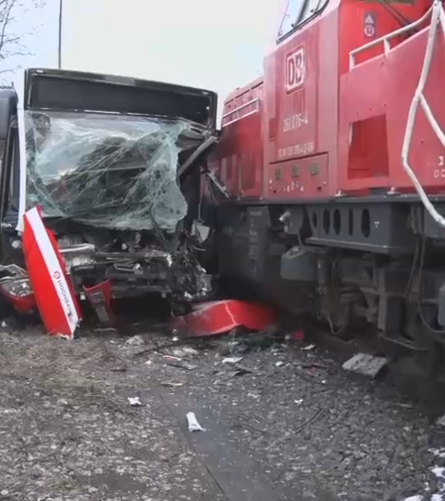 Rettungskräfte der Feuerwehr arbeiten an einer komplett zerstörten Glasfront eines Busses, der mit einer Rangierlokomotive kollidiert ist.