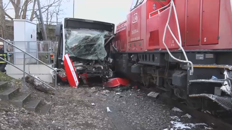 Rettungskräfte der Feuerwehr arbeiten an einer komplett zerstörten Glasfront eines Busses, der mit einer Rangierlokomotive kollidiert ist.