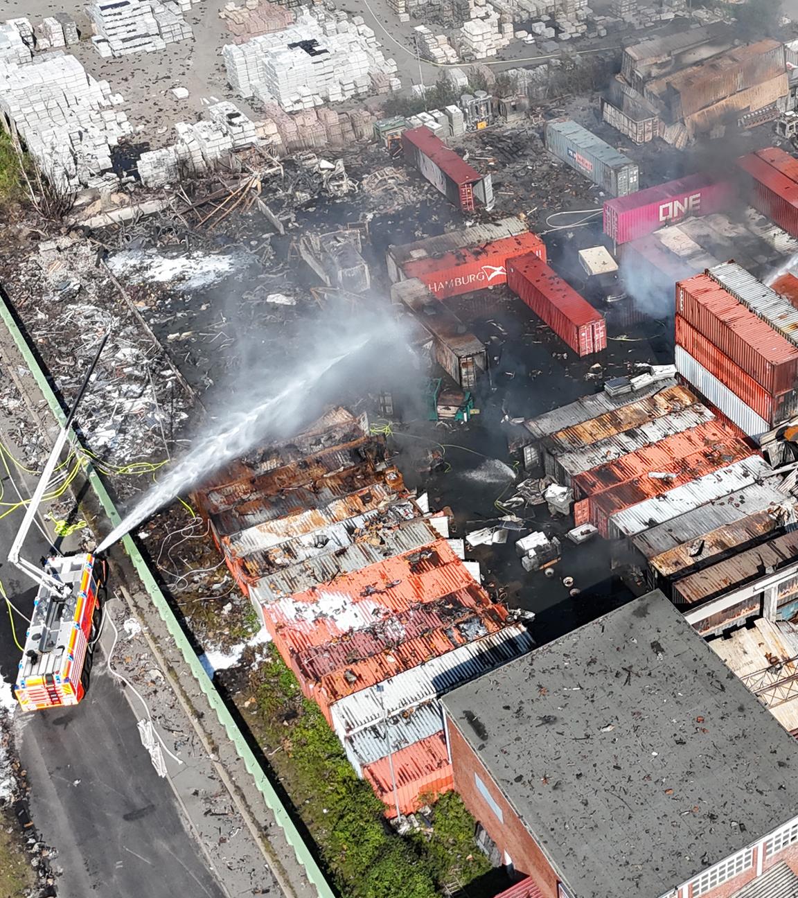 26.08.2025, Hamburg: Einsatzkräfte der Feuerwehr löschen einen Brand in einem Industriegebiet im Hamburger Hafen, in dem am Vortag ein Großbrand ausgebrochen war. 