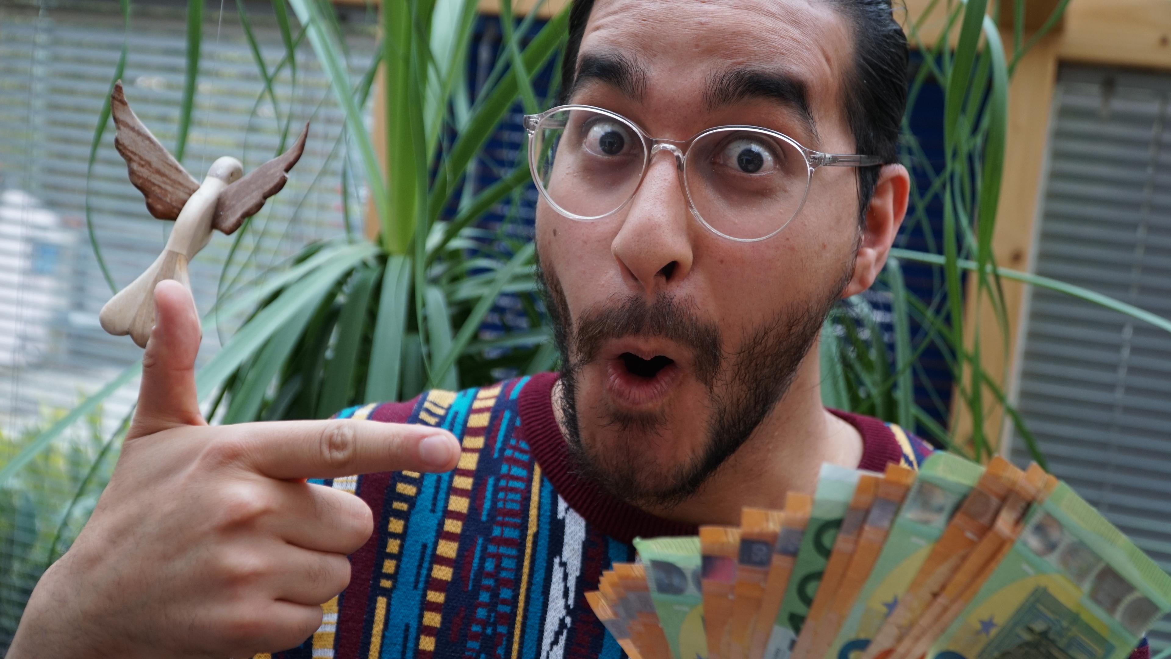 Ein junger Mann hält fröhlich-staunend ein Bündel Gelscheine in der Hand.
