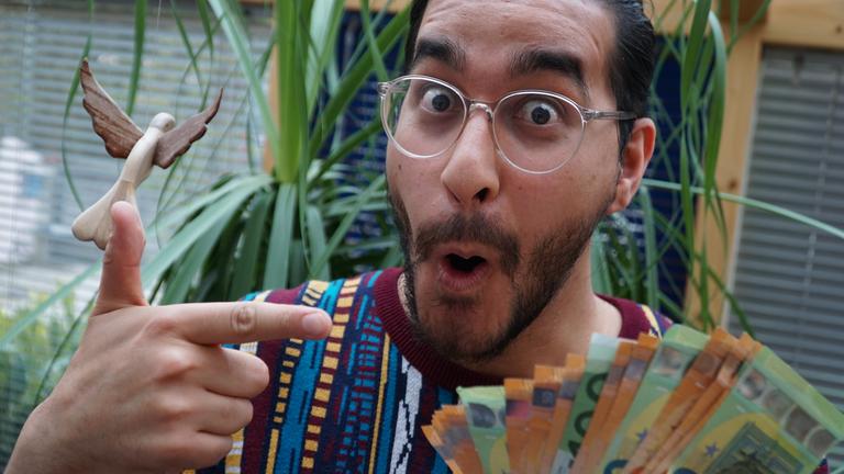 Ein junger Mann hält fröhlich-staunend ein Bündel Gelscheine in der Hand.