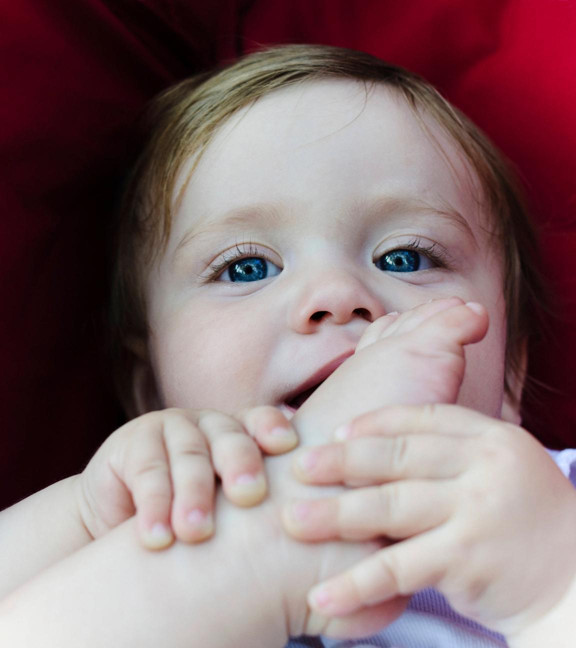 Ein Baby im Kinderwagen hält seinen Fuß in den Händen.