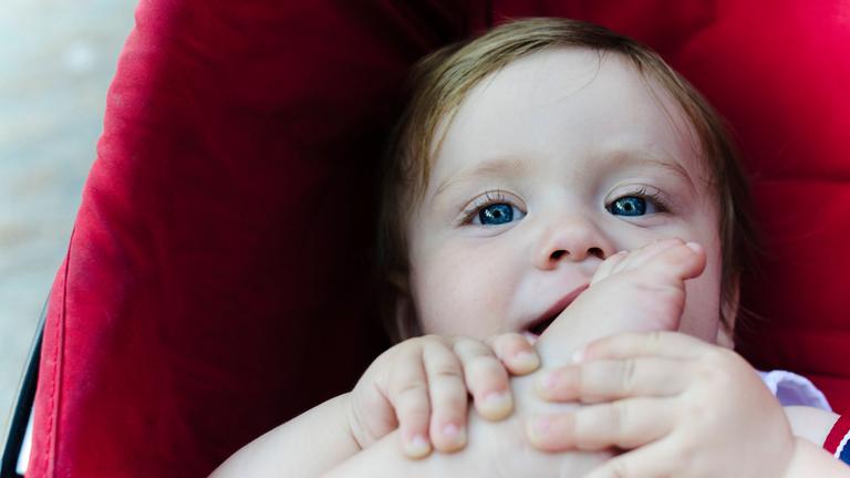 Ein Baby im Kinderwagen hält seinen Fuß in den Händen.