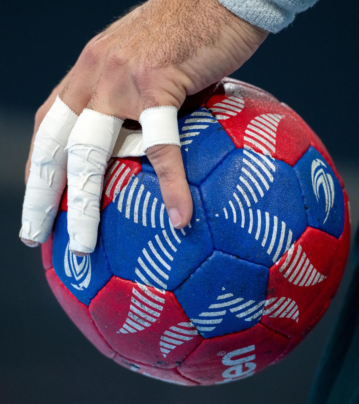 Eine Hand mit bandagierten Fingern hält einen Handball.