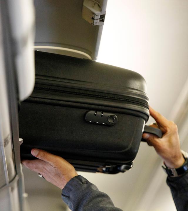 Ein Mann verstaut einen Kabinenkoffer im Gepäckfach der Flugzeugkabine.