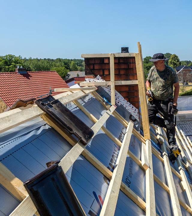 Ein Mitarbeiter einer Dachdeckerfirma steht für Arbeiten auf einem Dach.