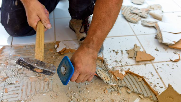 Ein Fliesenleger klopft Bodenfliesen ab.