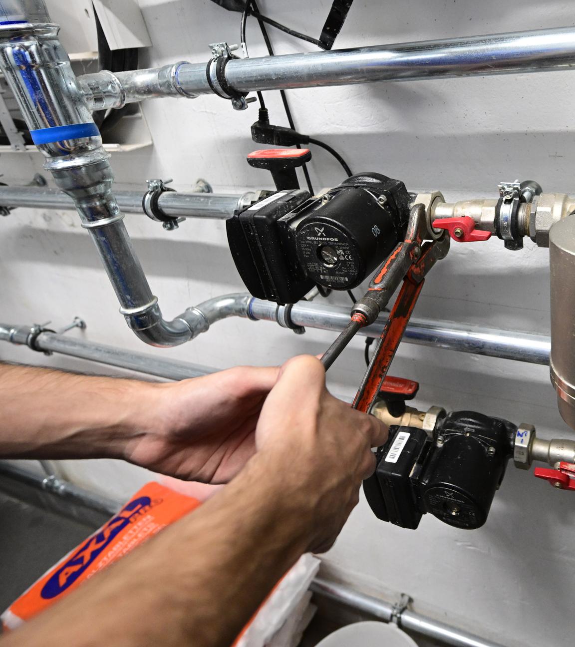  Ein Mitarbeiter in einem Handwerksbetrieb für Heizungsbau arbeitet in einem Heizungskeller eines Sportheims an der Installation der Technik für eine Wärmepumpe.