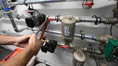  Ein Mitarbeiter in einem Handwerksbetrieb für Heizungsbau arbeitet in einem Heizungskeller eines Sportheims an der Installation der Technik für eine Wärmepumpe.