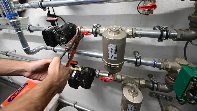  Ein Mitarbeiter in einem Handwerksbetrieb für Heizungsbau arbeitet in einem Heizungskeller eines Sportheims an der Installation der Technik für eine Wärmepumpe.