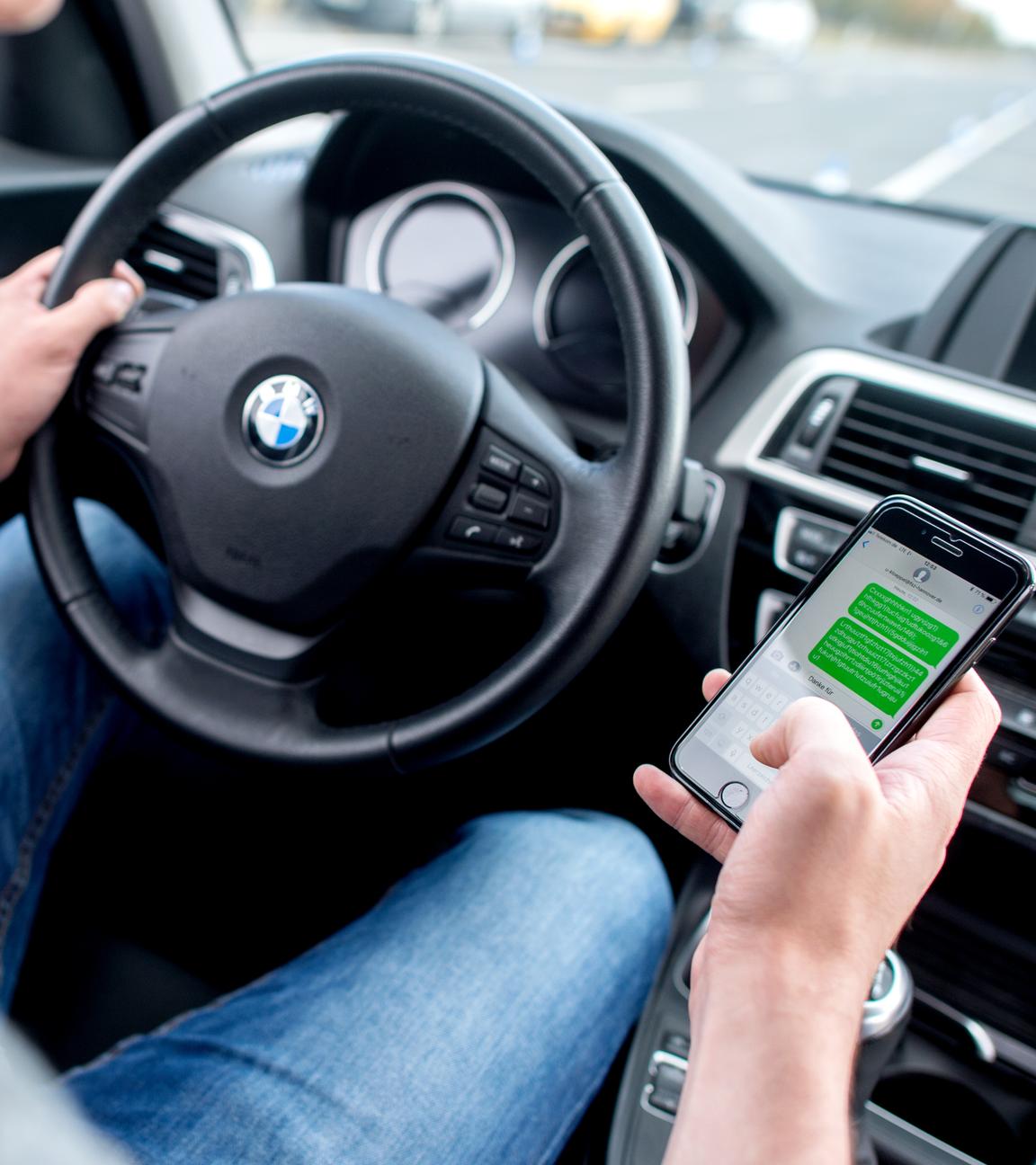 Ein Autofahrer schaut auf sein Smartphone während der Fahrt.