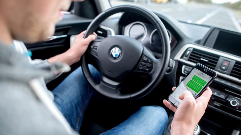 Ein Autofahrer schaut auf sein Smartphone während der Fahrt.