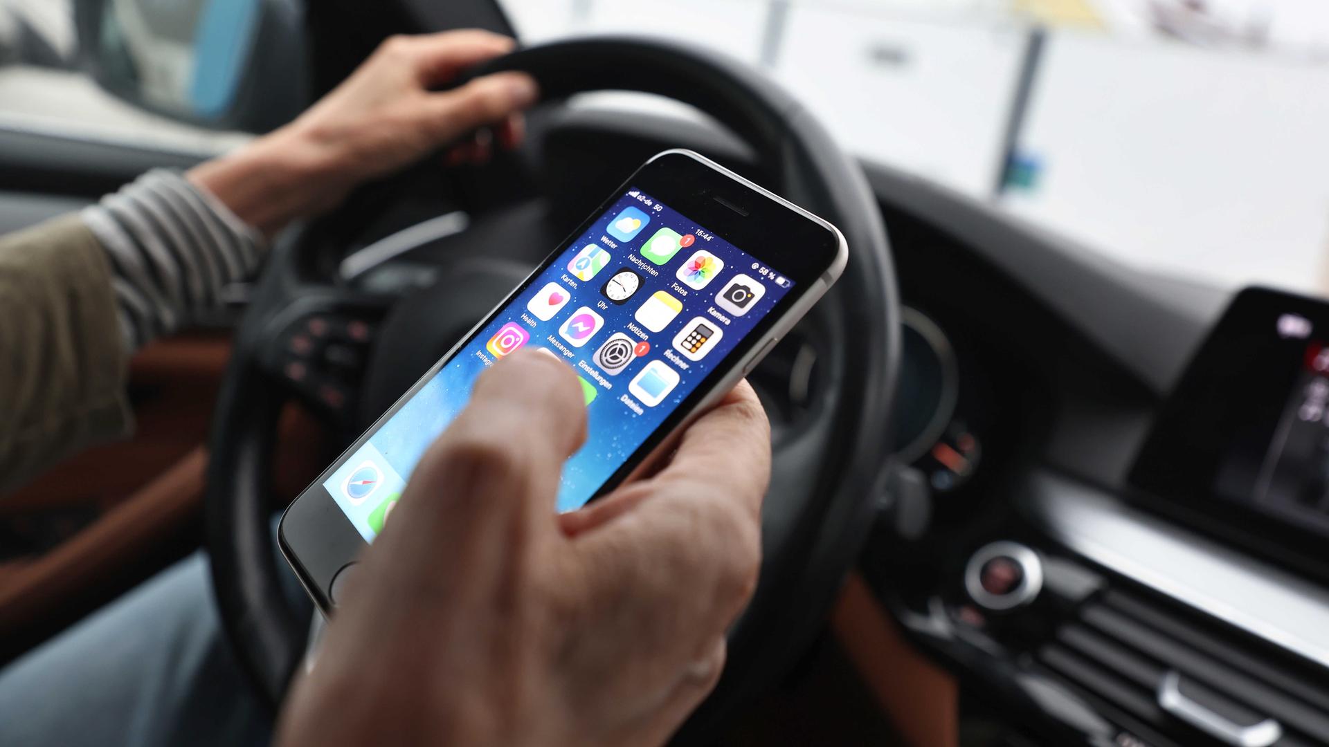 Ein Mann wirft einen Blick aufs Handy, während er am Steuer sitzt.