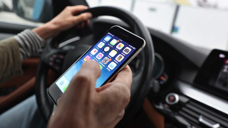 Ein Mann wirft einen Blick aufs Handy, während er am Steuer sitzt.