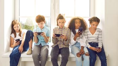Kinder sitzen nebeneinander und schauen auf Smartphones - Symbolbild
