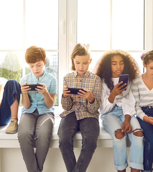Kinder sitzen nebeneinander und schauen auf Smartphones - Symbolbild