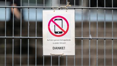 08.04.2025, Baden-Württemberg, Stuttgart: Ein Schild mit einem durchgestrichenen Smartphone und der Aufschrift "Auf dem ganzen Schulgelände - zu jeder Uhrzeit! DANKE!" hängt am Zugangstor zum Schulhof eines Gymnasiums und weist auf ein generelles Handyverbot hin.