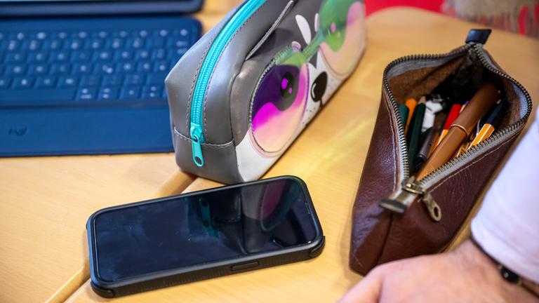 28.02.2024, Bremen: Ein Tablet und Handy liegen an einer Schule im Unterricht am Platz einer Schülerin.