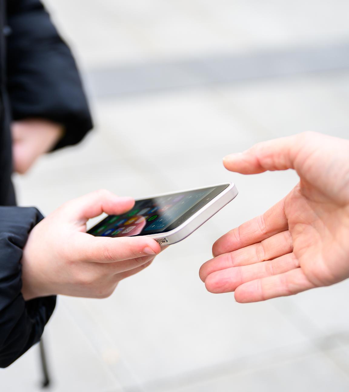 Ein Schüler gibt sein Handy einer anderen Person in die Hand. 
