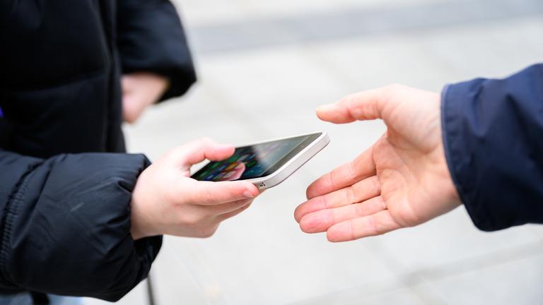Ein Schüler gibt sein Handy einer anderen Person in die Hand. 