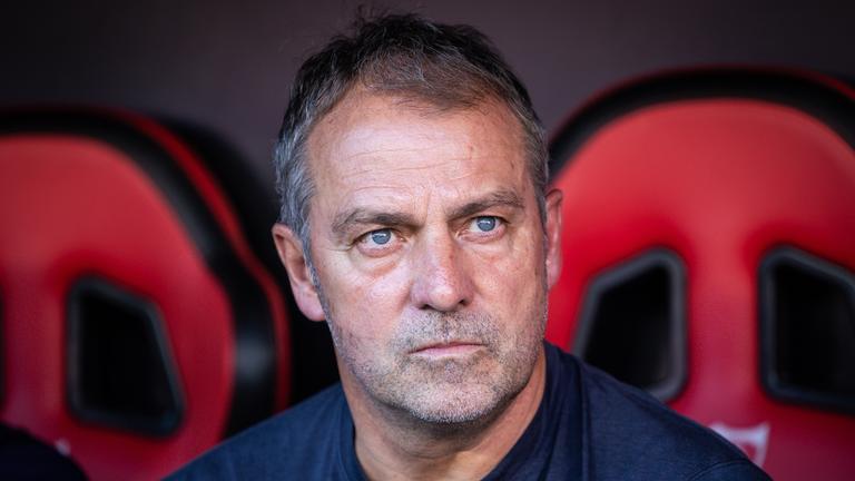 Hansi Flick sitzt auf der Trainerbank und schaut nachdenklich 