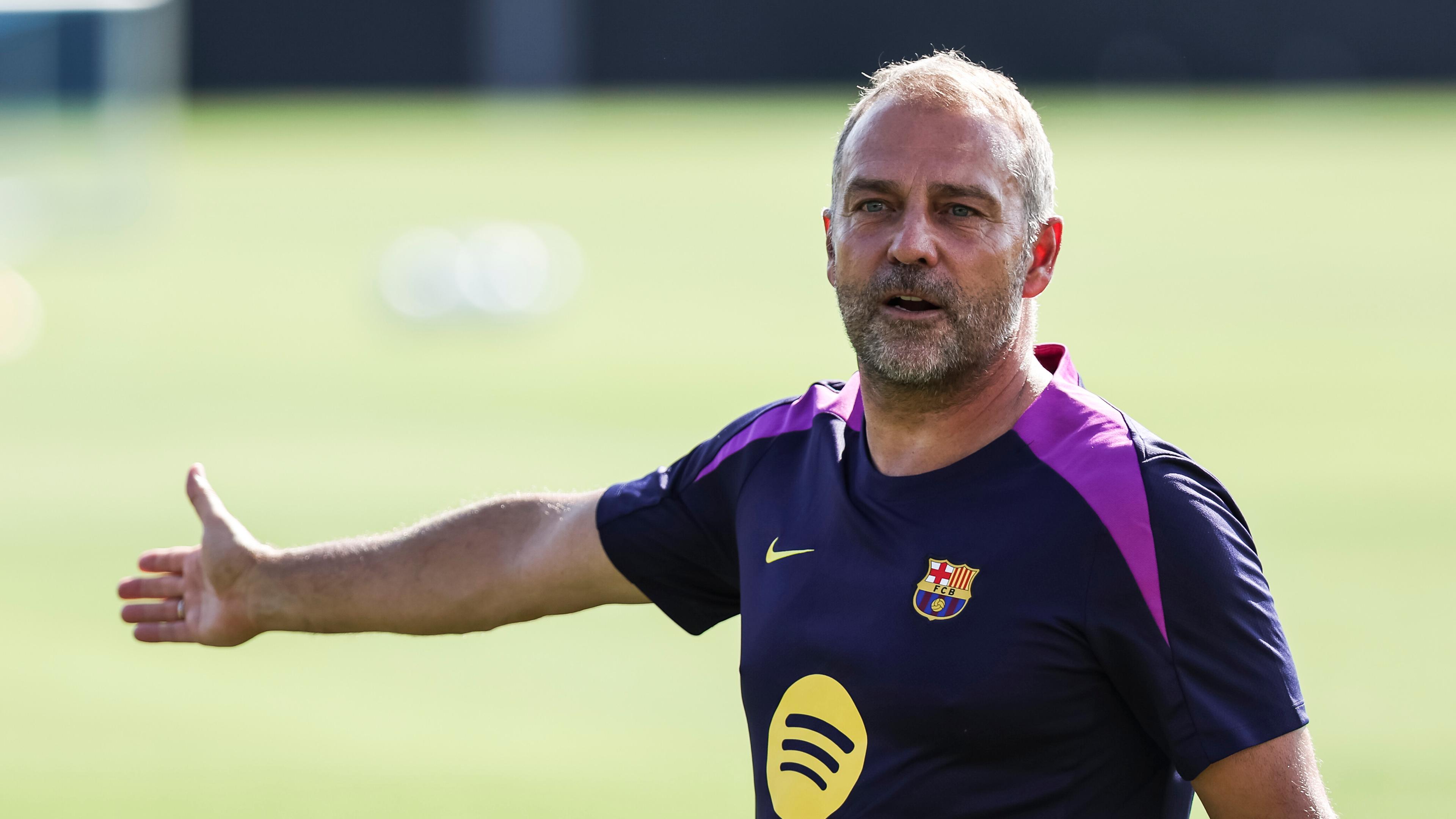 Der Trainer von FC Barcelona, Hansi Flick steht in einem Barcelona Trikot auf einem Fußballplatz.