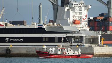Ein kleines rotes Rettungsboot, darin Menschen in Schutzkleidung, vor dem Kreuzfahrtschiff. 
