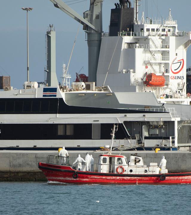 Ein kleines rotes Rettungsboot, darin Menschen in Schutzkleidung, vor dem Kreuzfahrtschiff. 