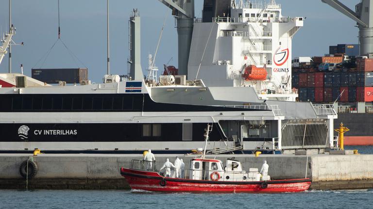 Ein kleines rotes Rettungsboot, darin Menschen in Schutzkleidung, vor dem Kreuzfahrtschiff. 