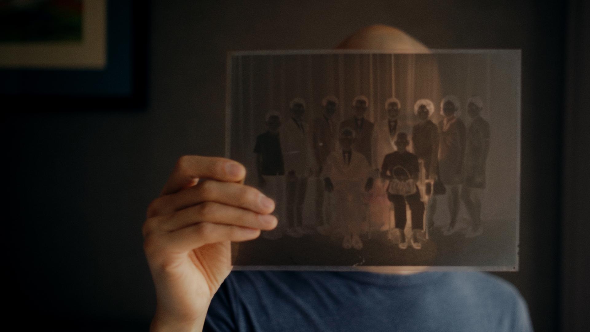 "Hao Are You": Regisseur Dieu Hao Do in einer Nahaufnahme. Er blickt durch ein Negativ eines Familienfotos, welches er in seiner Hand hält.