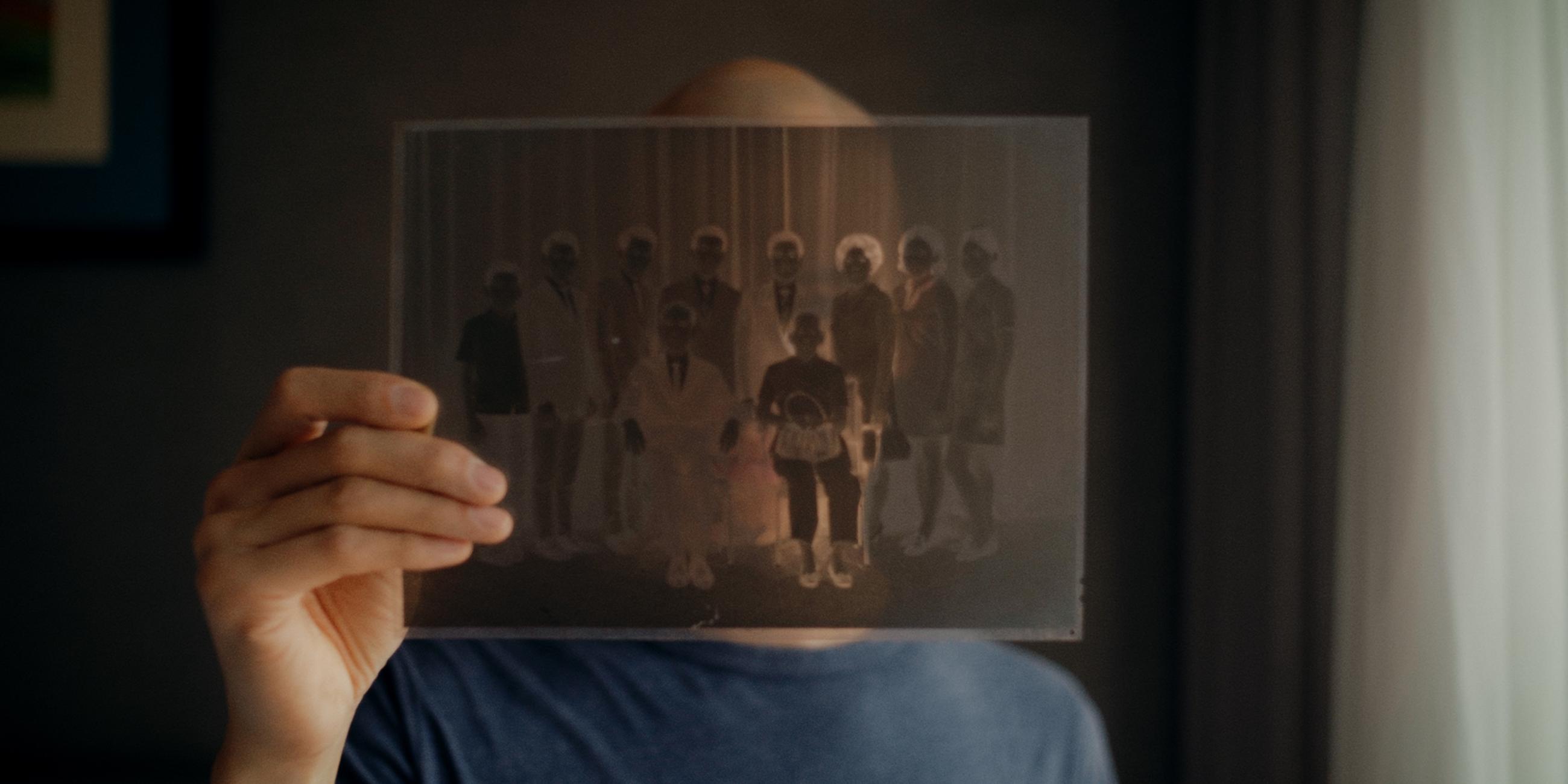 "Hao Are You": Regisseur Dieu Hao Do in einer Nahaufnahme. Er blickt durch ein Negativ eines Familienfotos, welches er in seiner Hand hält.