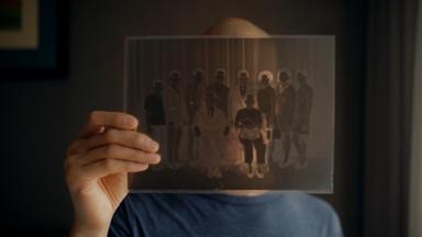 "Hao Are You": Regisseur Dieu Hao Do in einer Nahaufnahme. Er blickt durch ein Negativ eines Familienfotos, welches er in seiner Hand hält.