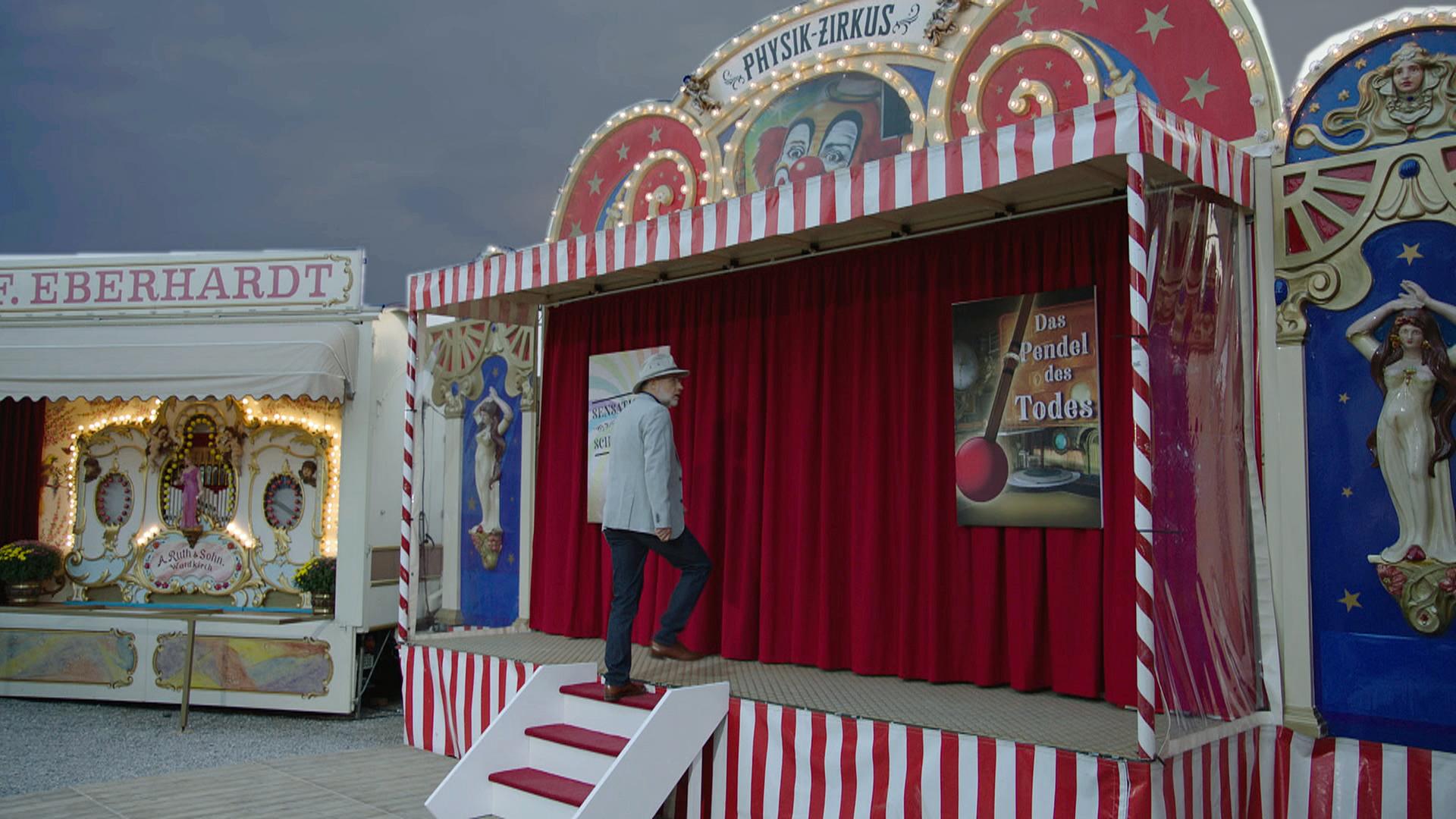 Harald Lesch betritt Jahrmarktbude namens "Physik-Zirkus"
