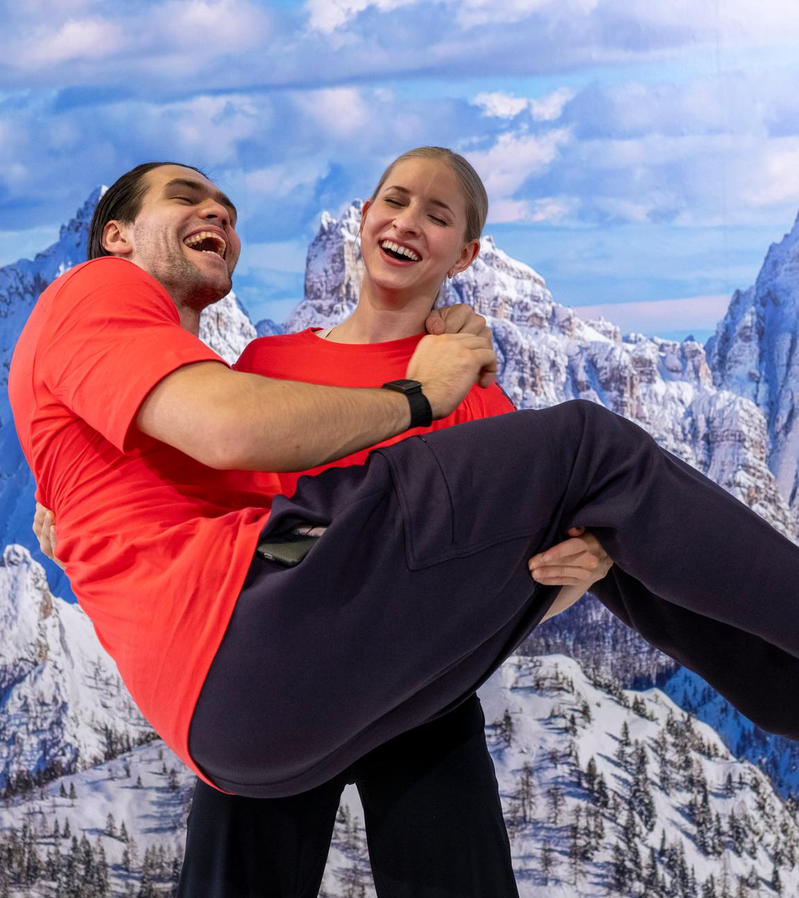 Die Eiskunstläufer Minerva Fabienne Hase und Nikita Volodin stehen während der Einkleidung für die Winterspiele in Mailand vor einer Fototapete zusammen.