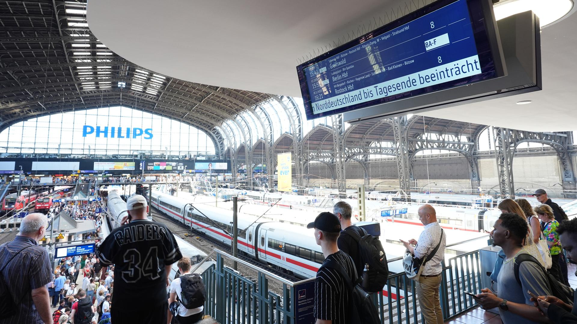 Hamburg: Bahnreisende stehen an den Bahnsteigen im Hamburger Hauptbahnhof, während auf einer Anzeigetafel auf den beeinträchtigten Bahnverkehr  hingewiesen wird