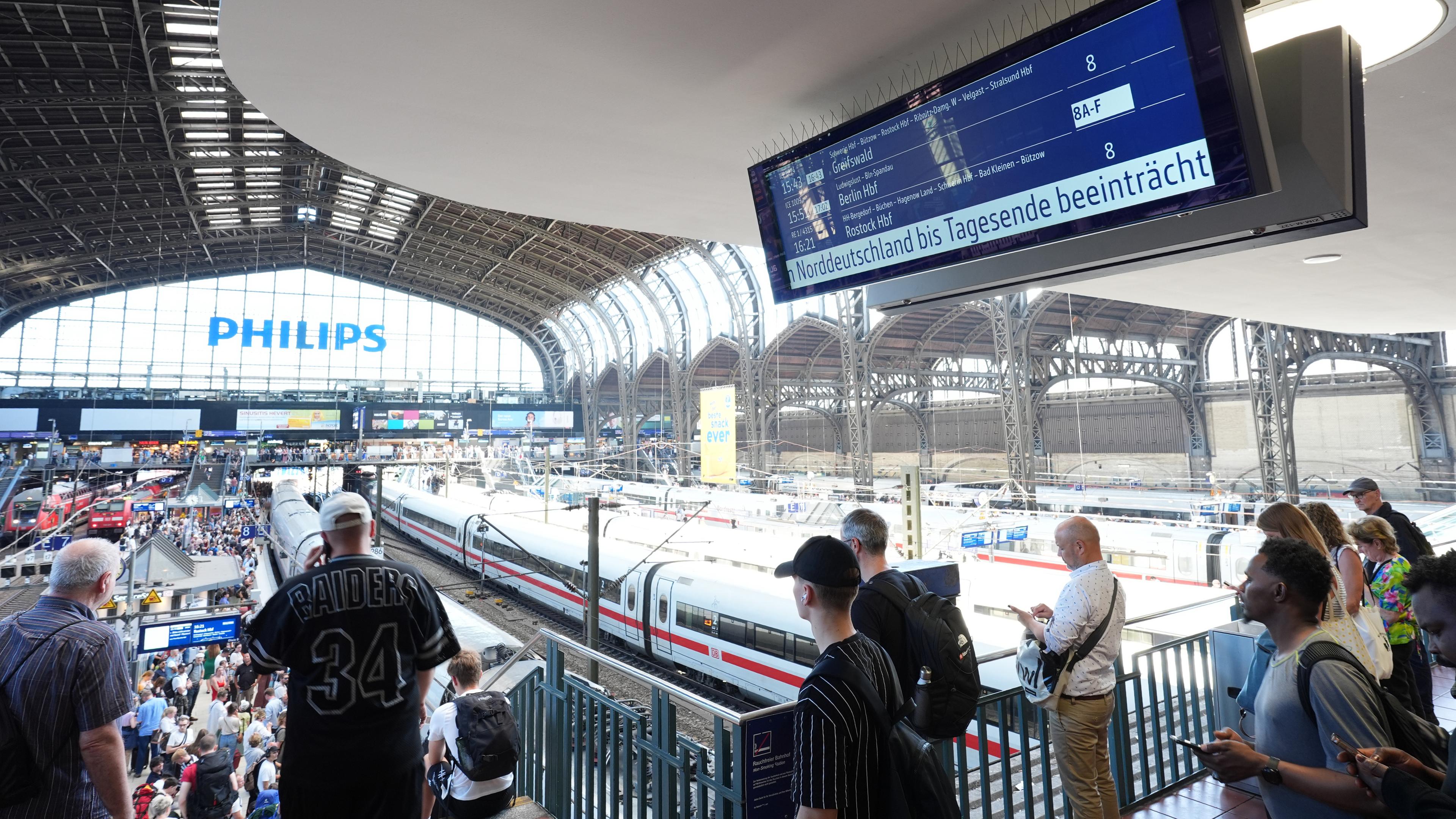 Hamburg: Bahnreisende stehen an den Bahnsteigen im Hamburger Hauptbahnhof, während auf einer Anzeigetafel auf den beeinträchtigten Bahnverkehr  hingewiesen wird
