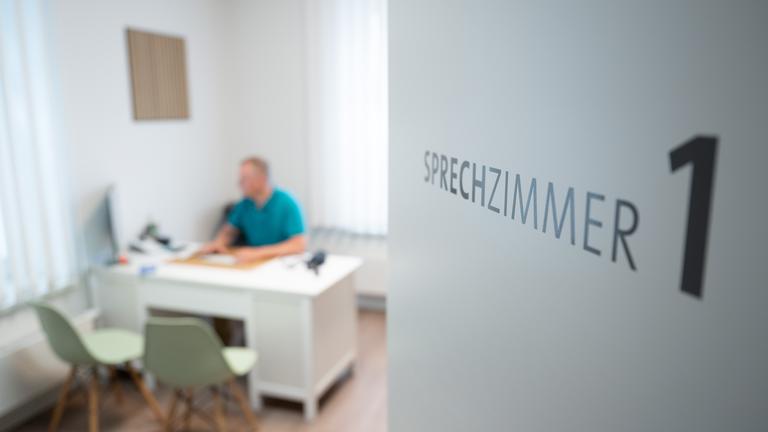 Ein Hausarzt sitzt in einem Sprechzimmer seiner Hausarztpraxis an einem Schreibtisch und arbeitet am Computer. 