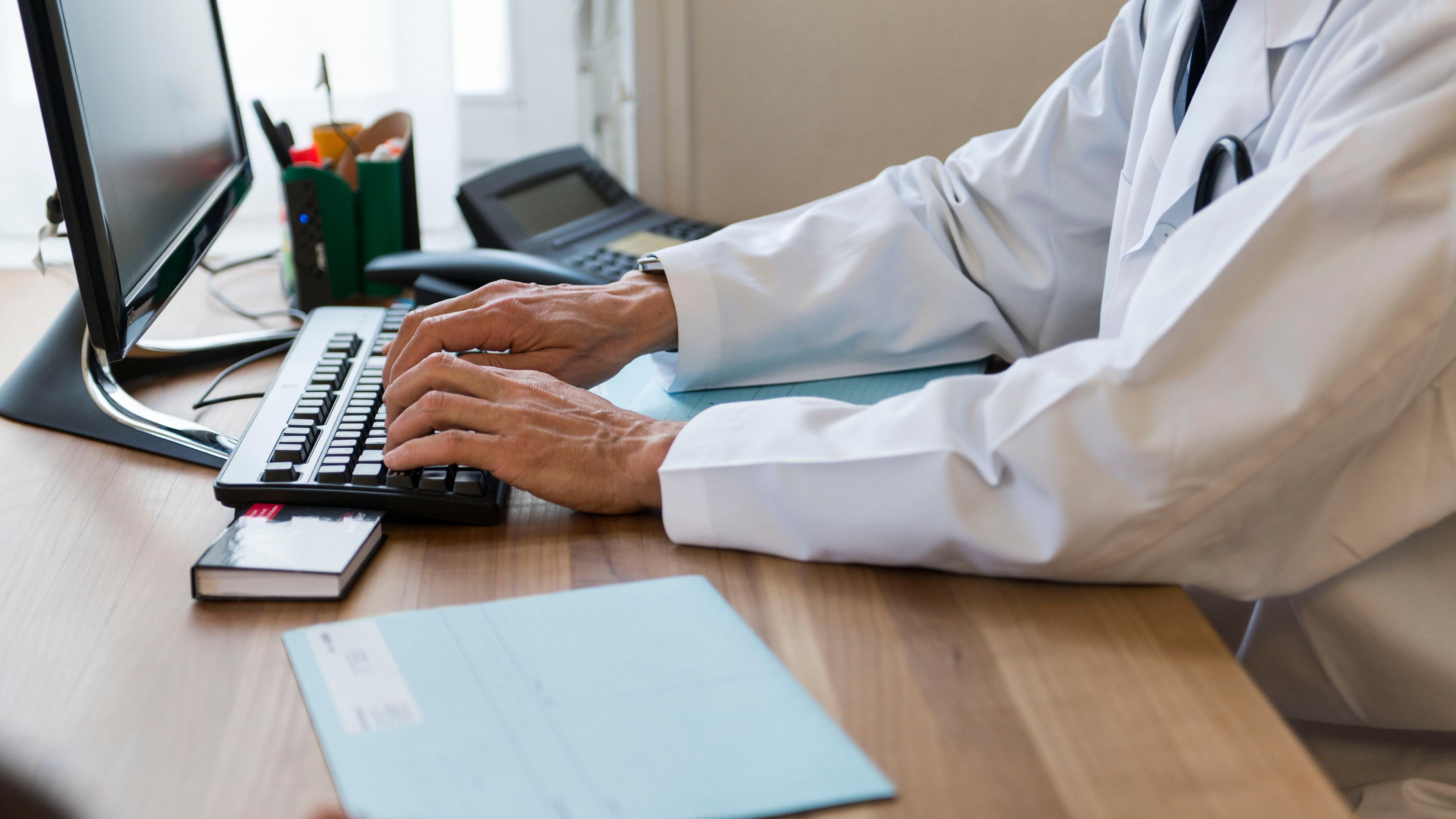 Ein Arzt sitzt während einer Besprechung mit einem Patienten an seinem Computer.