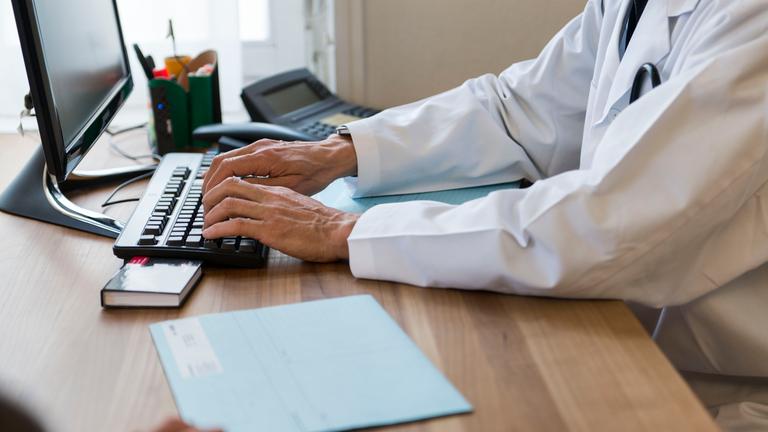 Ein Arzt sitzt während einer Besprechung mit einem Patienten an seinem Computer.