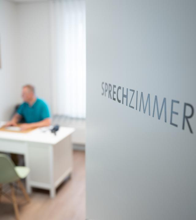 Ein Hausarzt sitzt in einem Sprechzimmer seiner Hausarztpraxis an einem Schreibtisch und arbeitet am Computer.