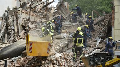 Einsatzkräfte von Feuerwehr und Technischem Hilfswerk arbeiten in den Trümmern eines eingestürzten Gebäudes.