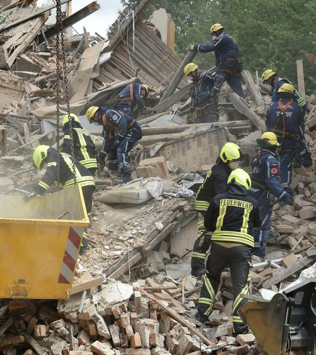 Einsatzkräfte von Feuerwehr und Technischem Hilfswerk arbeiten in den Trümmern eines eingestürzten Gebäudes.