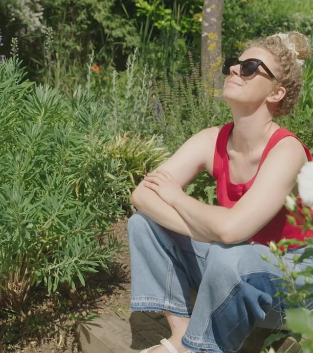 Eine Frau sitzt im Garten und genießt die Sonne.