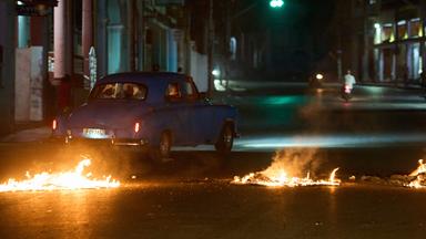 Menschen fahren mit einem amerikanischen Oldtimer durch eine Barrikade, die von Anwohnern errichtet wurde, die gegen anhaltende Stromausfälle in Havanna protestieren.