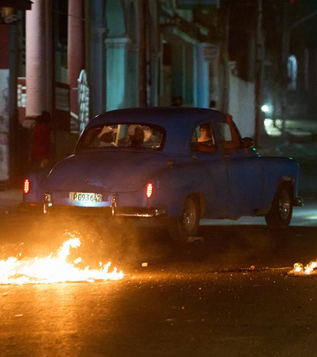 Menschen fahren mit einem amerikanischen Oldtimer durch eine Barrikade, die von Anwohnern errichtet wurde, die gegen anhaltende Stromausfälle in Havanna protestieren.