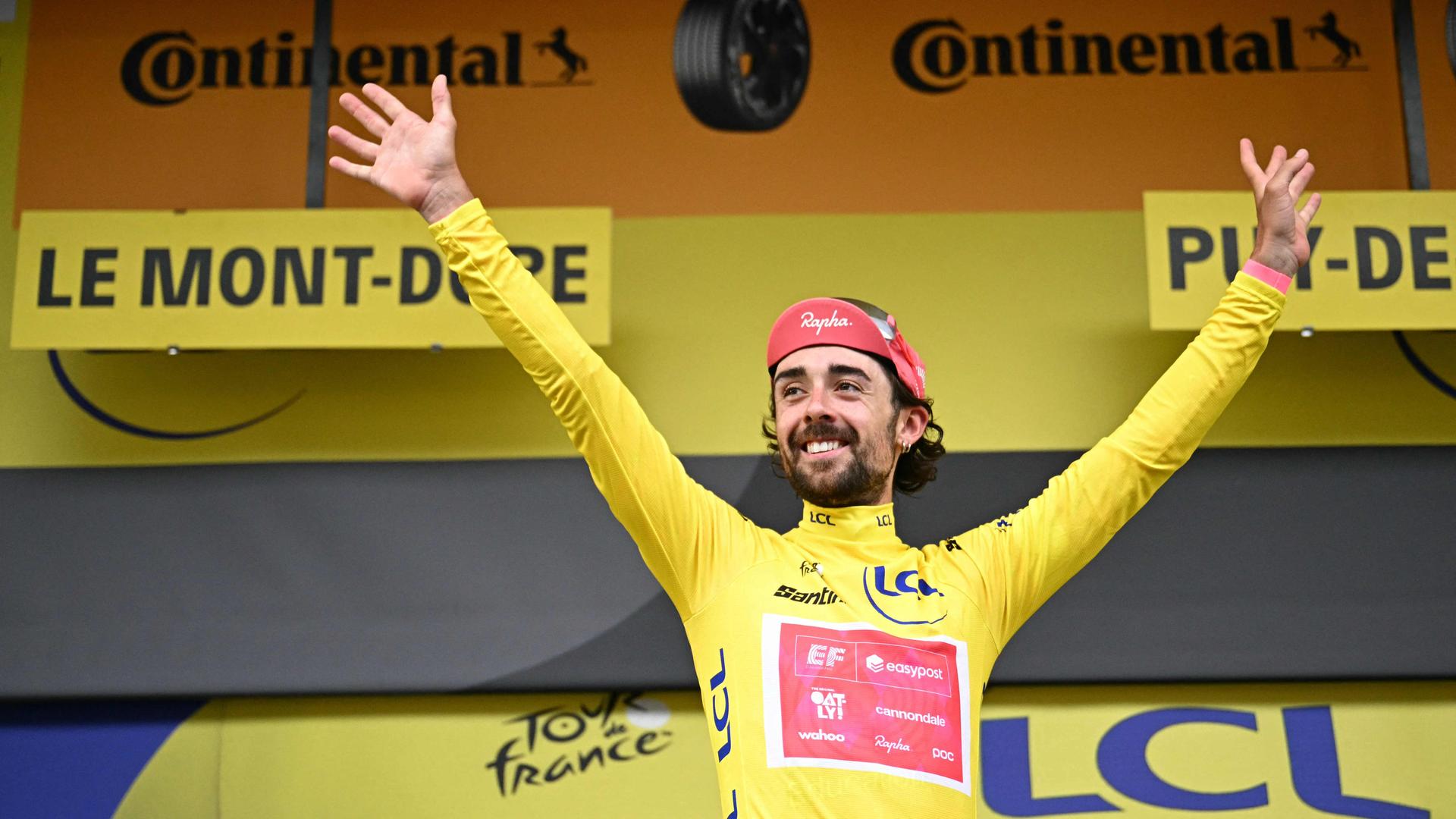 Ben Healy breitet im Gelben Trikot auf dem Podium die Arme aus.