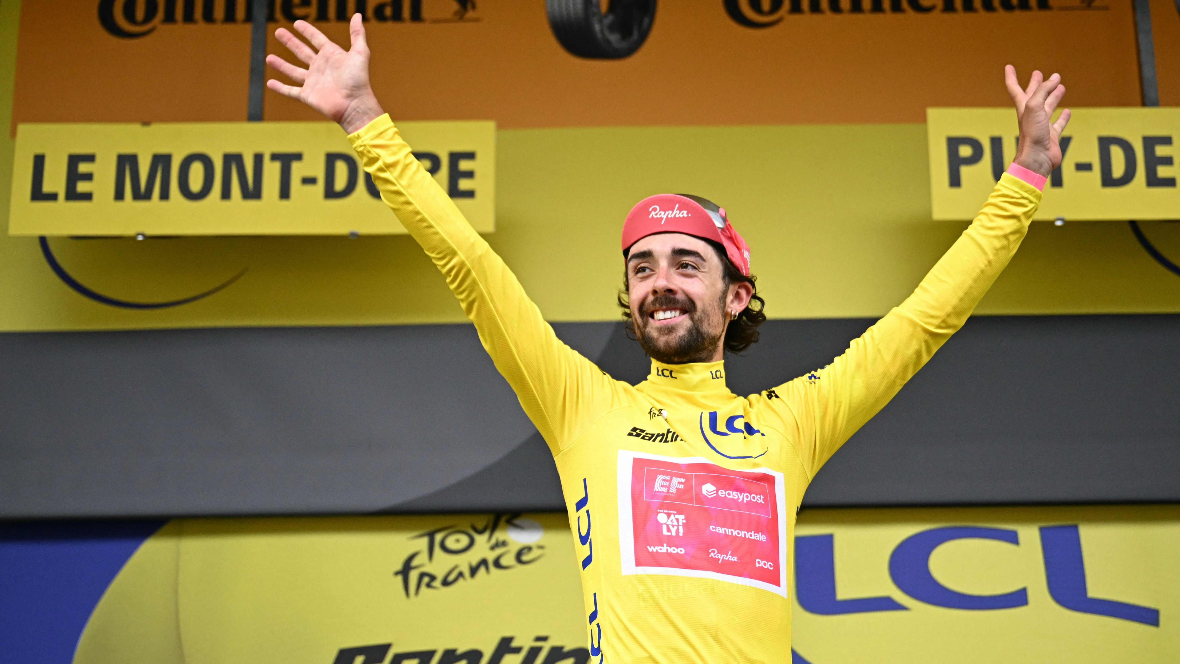 Ben Healy breitet im Gelben Trikot auf dem Podium die Arme aus.