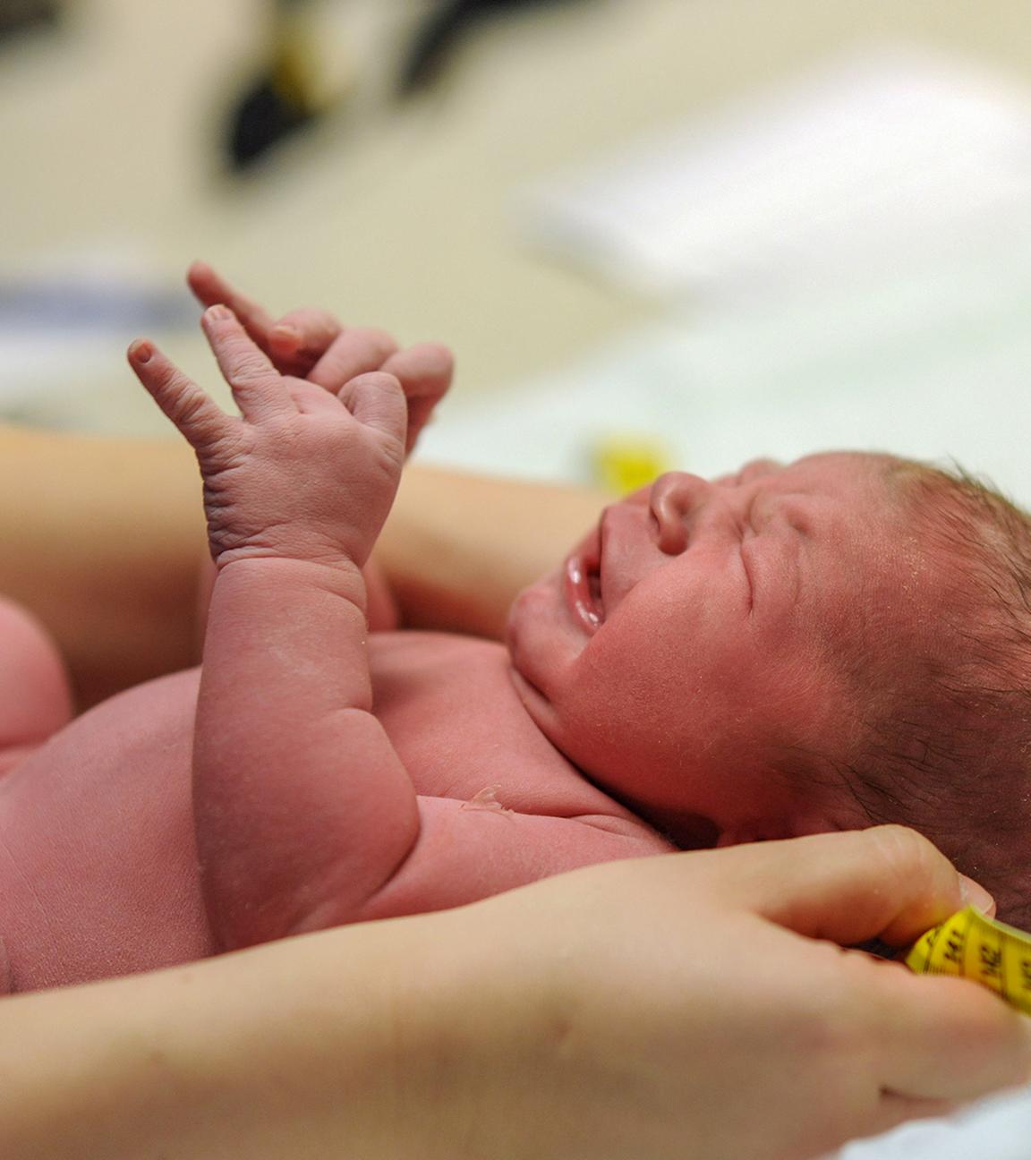 Neugeborenes wird in den Händen einer Hebamme gehalten