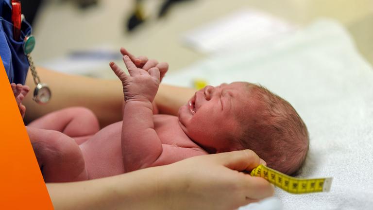 Neugeborenes wird in den Händen einer Hebamme gehalten