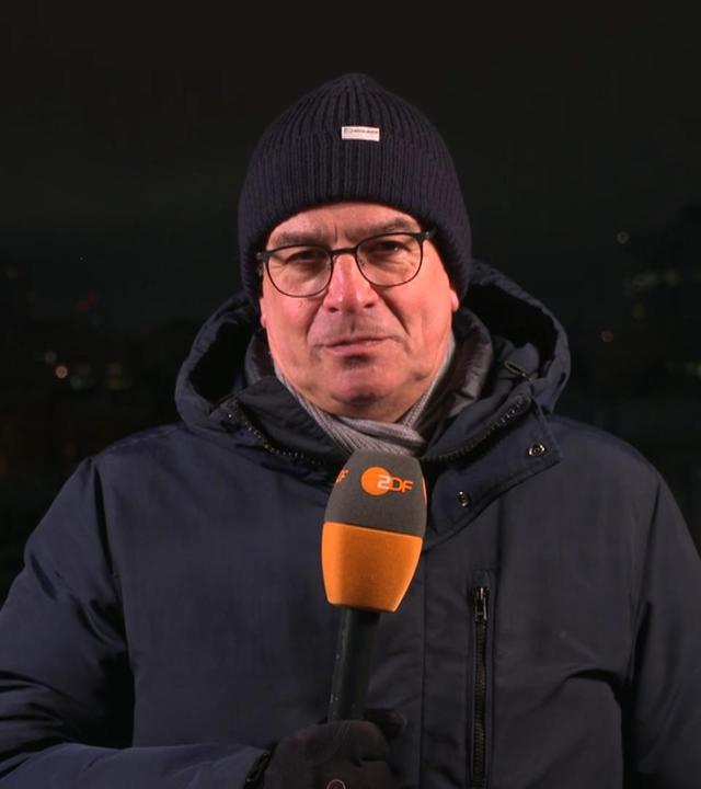 ZDF-Reporter Henner Hebestreit vor dunklem Hintergrund mit Mikrofon